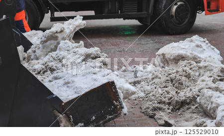 Tractor shovel loading dirty snow into a truck during snow removal in winter 125529010