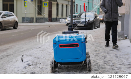 Autonomous delivery robot moving on a snowy sidewalk in Moscow. Autonomous delivery robot moving on a snowy sidewalk in Moscow. 125529067
