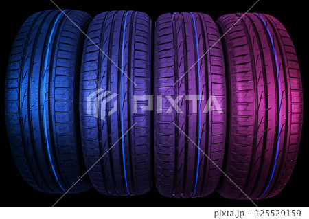 Studio shot of a set of summer car tires in pink and blue tones. Tire stack background. Car tyre protector close up. Black rubber tire. Brand new car tires. Close up black tyre profile. Car tires in a 125529159