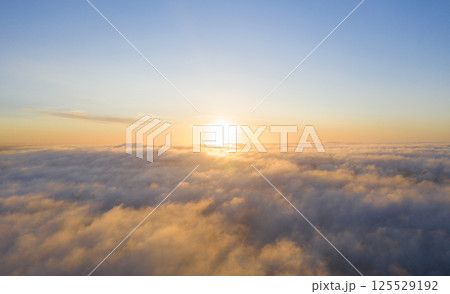 Aerial view gold sunrise over clouds in blue sky. Aerial top view cloudscape. Texture of clouds. View from above. Orange sunrise or sunset over clouds. Panorama clouds texture 125529192