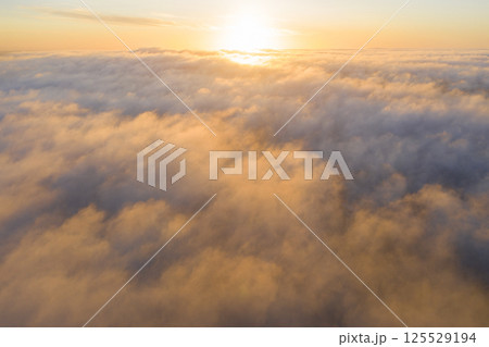 Aerial view gold sunrise over clouds in blue sky. Aerial top view cloudscape. Texture of clouds. View from above. Orange sunrise or sunset over clouds. Panorama clouds texture 125529194