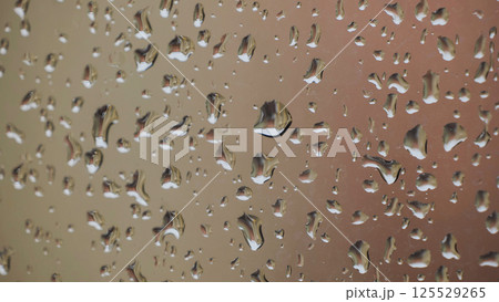 Raindrops sliding on a window during a rainy day reflecting a building 125529265