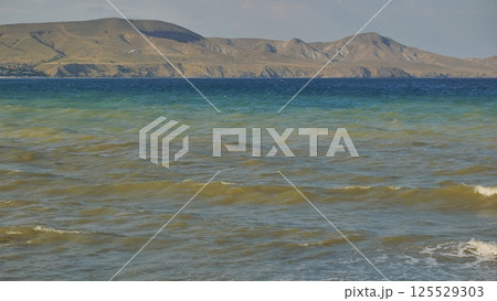 Gentle waves caressing sandy shoreline, tranquil black sea waters revealing distant crimean coastline under soft light 125529303