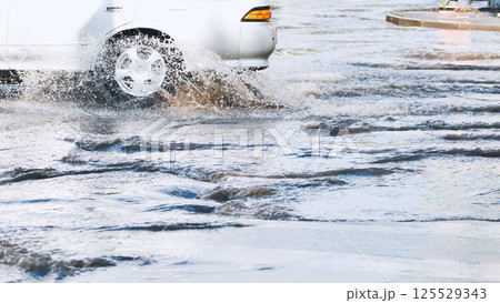 White car navigating a flooded street after heavy rain, sending up splashes and waves as water flows around the tires White car navigating a flooded street after heavy rain, sending up splashes and waves as water flows around the tires 125529343