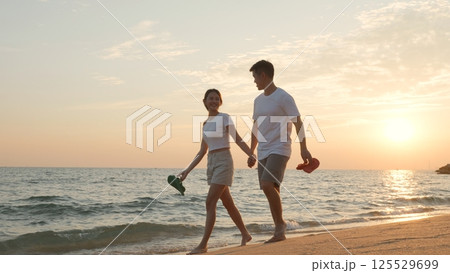 Vacation loving couple walking on beach together at sunset landscape, relaxing vacation travel summer, Asian man and woman in love holding hands walks along the sandy seashore 125529699