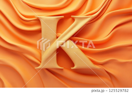 The letter K is made out of gold and is on a piece of orange fabric 125529782
