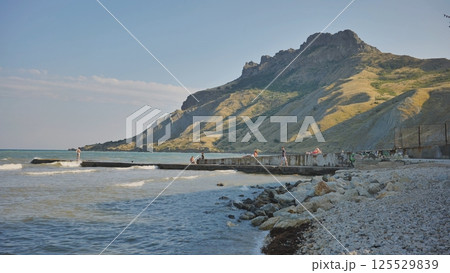 Tourists relaxing on Koktebel beach under Kara Dag mountain in Crimea Tourists relaxing on Koktebel beach under Kara Dag mountain in Crimea 125529839