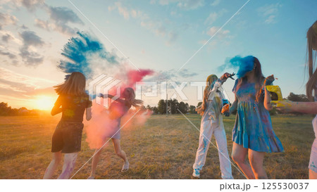 Happy school buddies having fun tossing colorful powder in the air at sunset in a park, marking their friendship and summer break 125530037