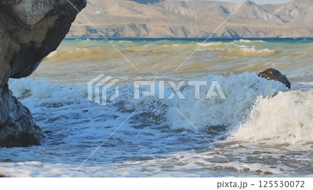Powerful waves striking rocky crimean shoreline, mountainous terrain rising behind azure waters Powerful waves striking rocky crimean shoreline, mountainous terrain rising behind azure waters 125530072