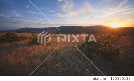 Crimean sunset illuminating dry meadow and distant mountains Crimean sunset illuminating dry meadow and distant mountains 125530158