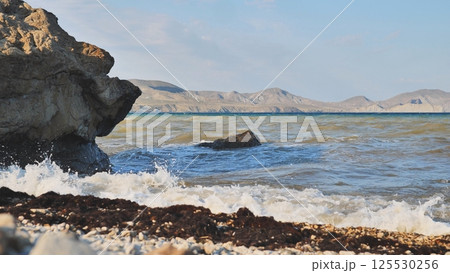 Foaming waves pounding rocky crimean shoreline with mountainous peninsula silhouette Foaming waves pounding rocky crimean shoreline with mountainous peninsula silhouette 125530256