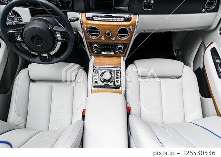 Modern luxury car white leather interior with natural wood panel. Part of leather car seat details with stitching. Interior of prestige modern car. White perforated leather. Car detailing. Car inside 125530336