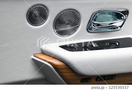 Door handle with power window control buttons of a luxury passenger car. White perforated leather interior with stitching and natural wood panel. Modern car interior details. Car detailing. Car inside 125530337