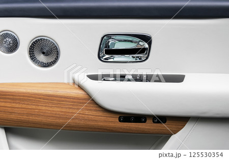 Door handle with power window control buttons of a luxury passenger car. White perforated leather interior with stitching and natural wood panel. Modern car interior details. Car detailing. Car inside Door handle with power window control buttons of a luxury passenger car. White perforated leather interior with stitching and natural wood panel. Modern car interior details. Car detailing. Car inside 125530354