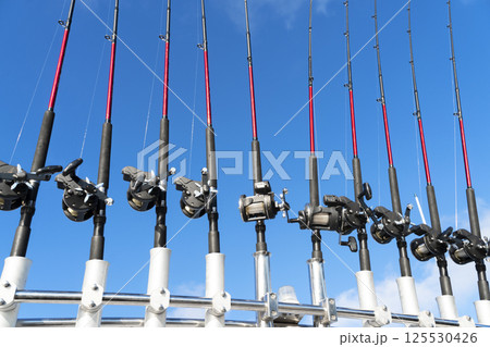 Fishing trolling boat rods in rod holder. Big game fishing. Fishing reels and rods pattern on boat. Sea fishing rods and reels in a row 125530426