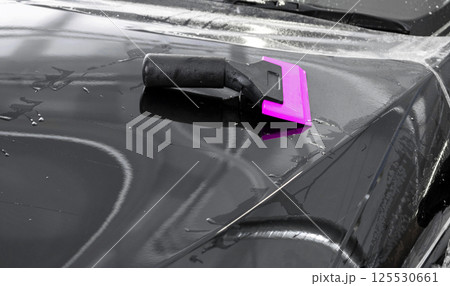 Car wrapping specialist putting vinyl foil or film on car. Protective film on the car. Applying a protective film to the car with tools. Car detailing. Transparent film. Car paint protection. Trimming 125530661