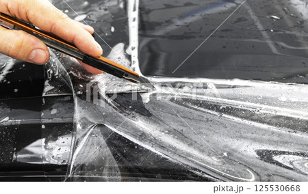 Car wrapping specialist cutting vinyl foil or film on car. Protective film. Applying a protective film with tools for work. Car detailing. Transparent film. Car paint protection. Trimming. Car wrapping specialist cutting vinyl foil or film on car. Protective film. Applying a protective film with tools for work. Car detailing. Transparent film. Car paint protection. Trimming. 125530668