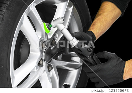 Car polish wax worker hands polishing car wheel. Buffing and polishing car disc. Car detailing. Man holds a polisher in the hand and polishes the car. 125530678