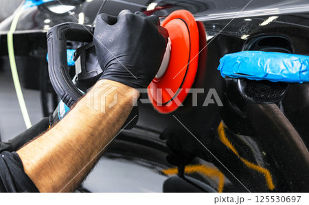 Car polish wax worker hands applying protective tape before polishing. Buffing and polishing car. Car detailing. Man holds a polisher in the hand and polishes the car Car polish wax worker hands applying protective tape before polishing. Buffing and polishing car. Car detailing. Man holds a polisher in the hand and polishes the car 125530697