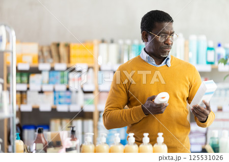 Thoughtful African American man choosing nourishing cream in drugstore 125531026