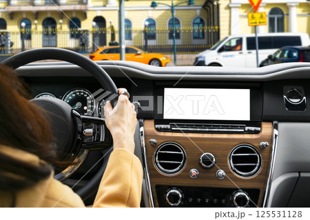 Woman hand holding car steering wheel in modern car. Hands on steering wheel of a car driving. Girl driving a car inside cabin. Monitor in car with isolated blank screen. Car display with blank screen 125531128