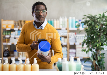 African man in pharmacy scans QR code on infant food. 125531421