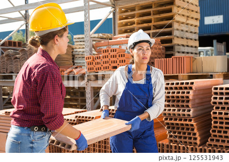 Construction warehouse female workers carry brick pallets on territory of open-air site 125531943