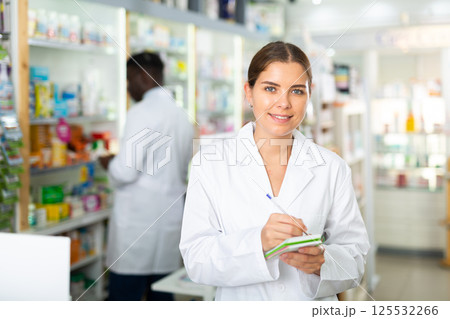 Young smiling female pharmacist making important notes in a notebook 125532266