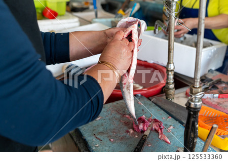 Fish being cleaned at a bustling market with vendors and fresh seafood during daytime Fish being cleaned at a bustling market with vendors and fresh seafood during daytime 125533360