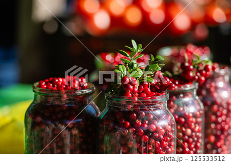 Freshly harvested red berries in glass jars at a vibrant farmers market during autumn 125533512