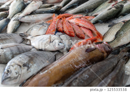 Multiple types of fish are lined up on ice at a lively market in the morning. Multiple types of fish are lined up on ice at a lively market in the morning. 125533538