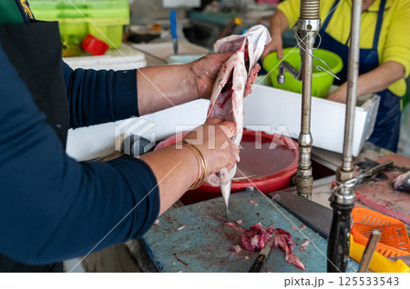 A person skillfully filleting fish at a bustling market stall during the morning hours. A person skillfully filleting fish at a bustling market stall during the morning hours. 125533543