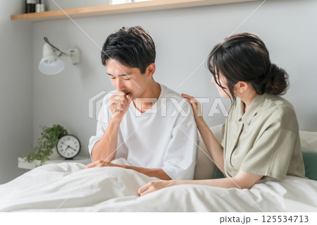 朝寝室で咳・風邪に悩む男性と心配する女性・夫婦・カップル 125534713