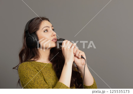cheerful young woman in casual clothes with headphones sing song in microphone, mock up copy space cheerful young woman in casual clothes with headphones sing song in microphone, mock up copy space 125535173