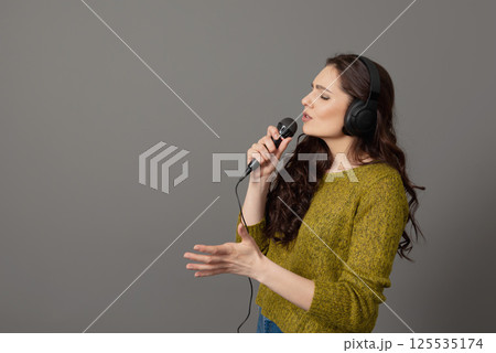 cheerful young woman in casual clothes with headphones sing song in microphone, mock up copy space cheerful young woman in casual clothes with headphones sing song in microphone, mock up copy space 125535174