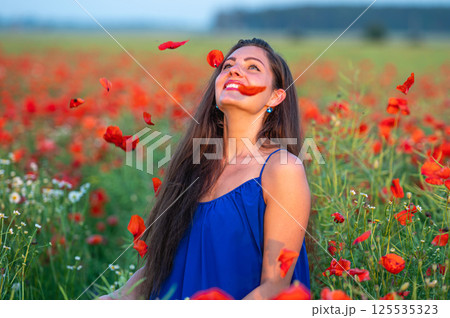 pretty young woman with long hair playing with petals in poppy field in evening sunlight 125535323