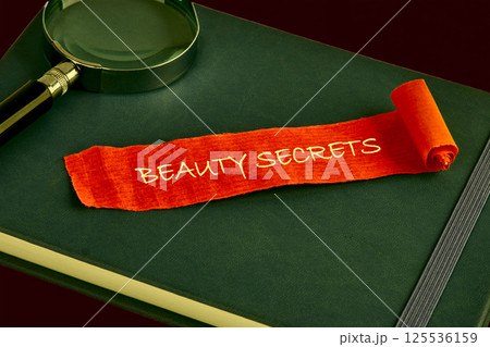 A vibrant piece of orange fabric features the words beauty secrets, resting on a green notebook alongside a magnifying glass, symbolizing the pursuit of wellness and beauty guidance A vibrant piece of orange fabric features the words beauty secrets, resting on a green notebook alongside a magnifying glass, symbolizing the pursuit of wellness and beauty guidance 125536159