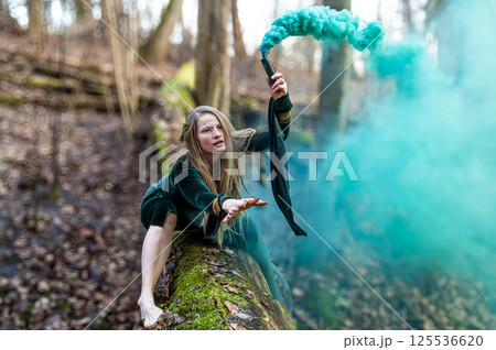 Woman holding smoke bomb in forest. Shallow depth of feld 125536620
