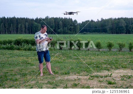 A man operating the drone by remote control on the meadow near forest. 125536961