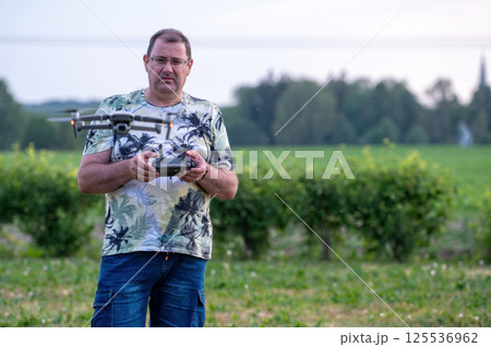 A man operating the drone by remote control on the meadow near forest. 125536962