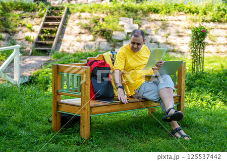 middle aged man with laptop and documents working outside in garden, green home office concept. middle aged man with laptop and documents working outside in garden, green home office concept. 125537442
