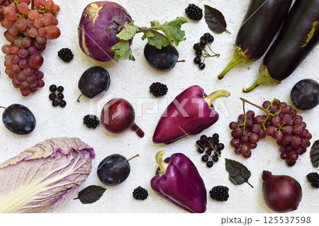 Flat lay of purple and black fruits and vegetables on a white background featuring grapes plums and eggplants perfect for healthy food promotions vegetarian recipes and colorful kitchen designs 125537598