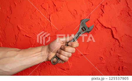 close up of muscular hand gripping spanner against vibrant red textured backdrop, showcasing strength and determination in striking visual close up of muscular hand gripping spanner against vibrant red textured backdrop, showcasing strength and determination in striking visual 125537905