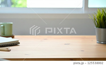 minimalist wooden table features stack of books, green coffee cup, and small potted plant, creating serene workspace atmosphere 125538002