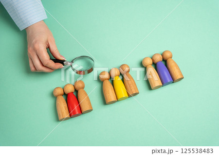 The concept of market segmentation. Target audience, customer care. Market group of buyers. Customer relationship management. Businessman looking through a magnifying glass at figurines of people 125538483