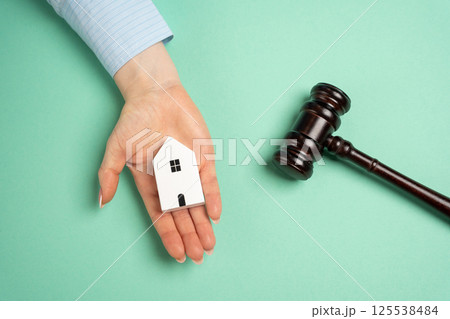 The female hand holding the wooden house and the judge's hammer. Real estate court decisions. Property inheritance litigation. Establishment of ownership. 125538484