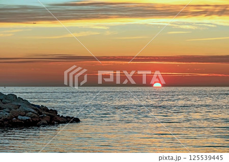 Peaceful Sunset Over the Sea.A breathtaking sunset paints the sky with vibrant orange, pink and purple hues, casting a golden glow over the calm sea waters.  125539445