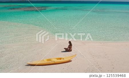 Aerial view of a serene moment on a pristine tropical beach, featuring a woman enjoying the tranquil atmosphere and a kayak resting on the soft, white sand 125539468