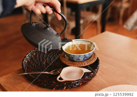 Hand pours green tea from a cast iron teapot 125539992