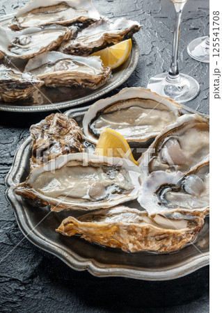 Fresh raw oysters on ice with lemon, on a black slate background Fresh raw oysters on ice with lemon, on a black slate background 125541708